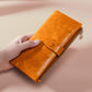 Orange leather zip wallet held in hand, front snap strap detail