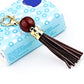 Gold-tone tassel keychain with dark red bead and dark brown leather tassel strands