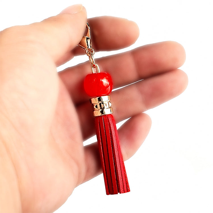 Red tassel keychain with round red bead and gold clasp, held in hand