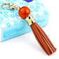 Gold-tone tassel keychain with orange bead and brown leather tassel strands