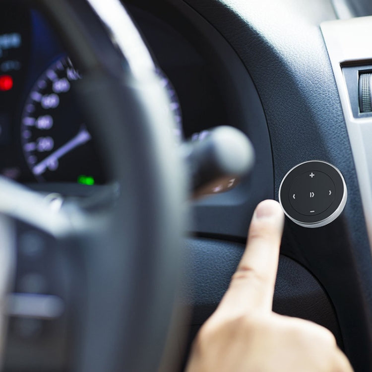 Black circular Bluetooth remote controller held by hand near car interior