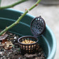 Perforated dark bonsai fertilizer dispenser with cover holding yellow pellets in pot