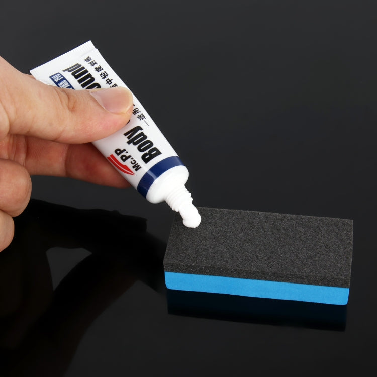 Hand applying car body compound onto dark gray abrasive sponge block