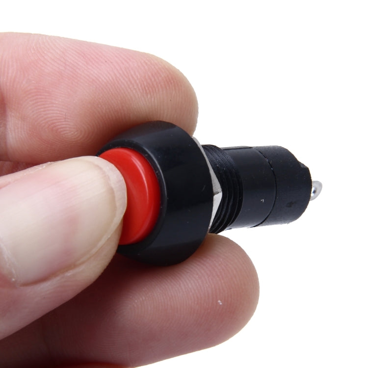 Thumb pressing red round push button on black 2-pin switch