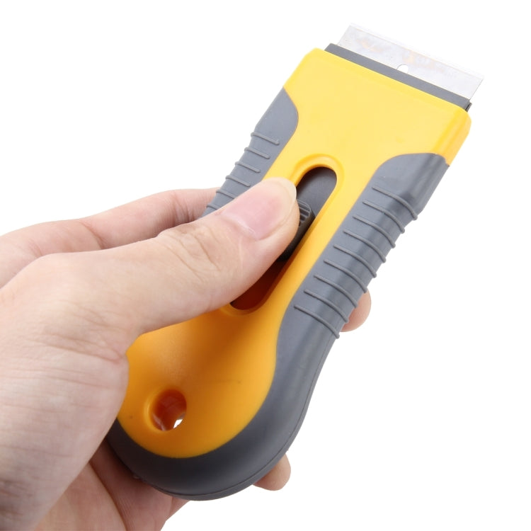 Window film scraper tool held in hand; yellow handle with exposed blade