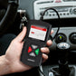 Black handheld OBD2 diagnostic code reader with lit screen held near car dashboard