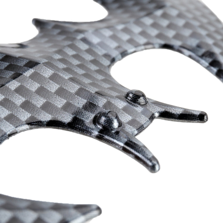 Close-up of bat-shaped metal car sticker: carbon-fiber texture with rivet details