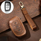 Brown leather key fob cover with stitched trim, brass key ring, and remote button cutouts
