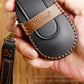 Black leather key fob case with tan insert, key ring, and contrast stitching.