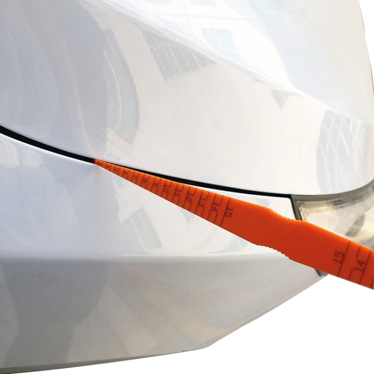 Orange car gap measurement ruler with scale across headlight area seam