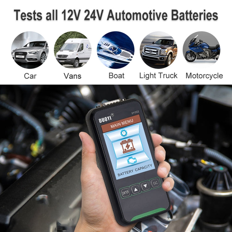 Handheld automotive battery tester with LCD display held in hand near engine