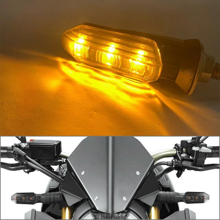 Black motorcycle LED turn signal light illuminated, amber glow through clear lens