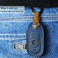 Blue leather key fob cover with tan strap and metal key ring on denim