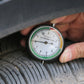 Tire tread depth gauge held to tire tread with pointer dial and scale in view