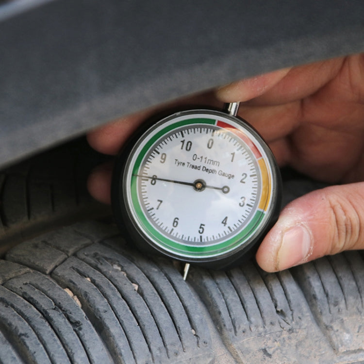 Tire tread depth gauge held to tire tread with pointer dial and scale in view