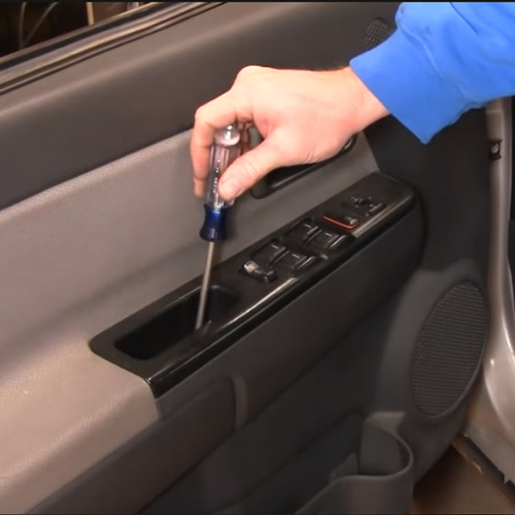 Window master switch installed in car door panel with hand using screwdriver