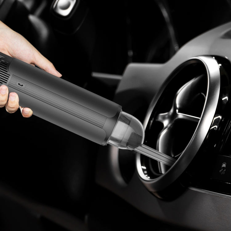 Hand holding handheld vacuum cleaner nozzle against car wheel area, dark gray