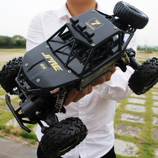 Black off-road RC climbing car being held; four oversized knobby tires and spring shocks
