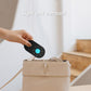 Compact black detector held above a bag, with a glowing blue status light.