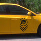 Skull-pattern emblem sticker on yellow car door, dark logo with circle, chevrons, and star