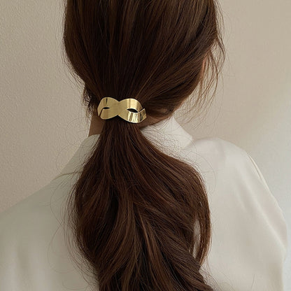 Gold metal bow hair tie with elastic band, holding long brown ponytail