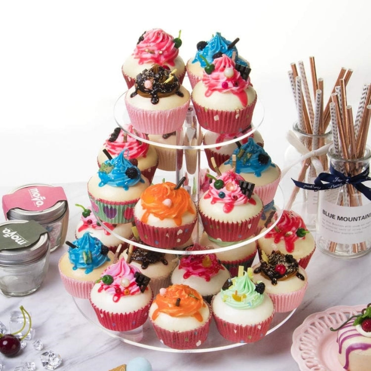 Three-tier clear acrylic cupcake stand with cupcakes and lidded jars nearby