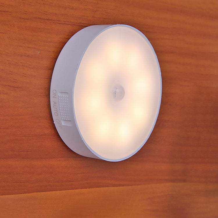 Round LED night light on wood surface, warm glowing white lens and gray outer ring