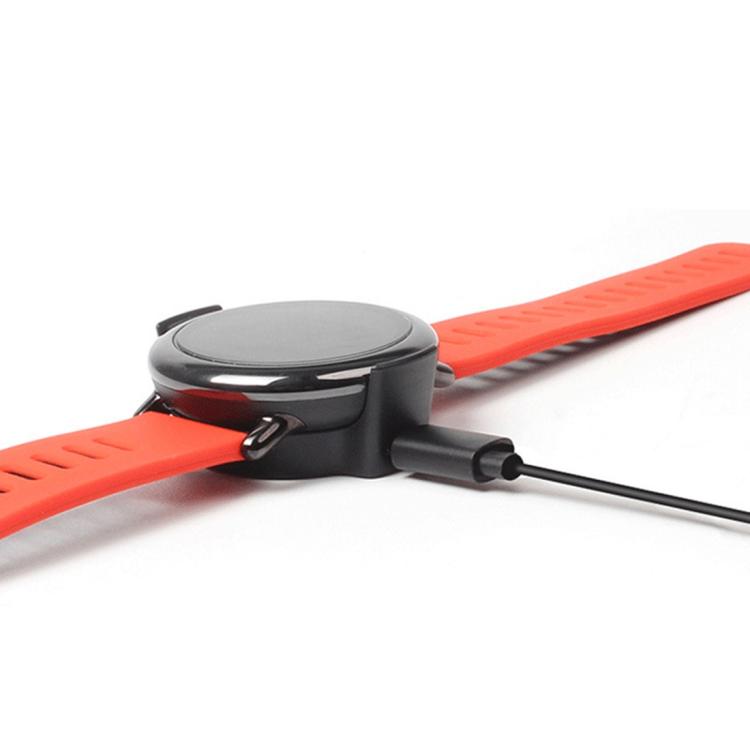 Black smartwatch seated in its charging cradle, connected by cable
