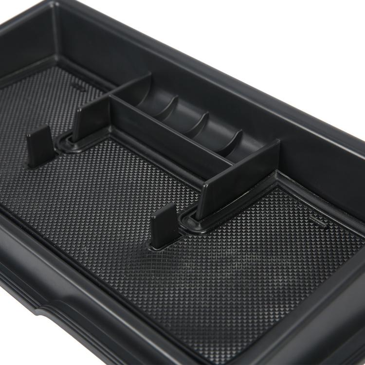 Black dashboard storage box interior with textured mat and raised storage slots