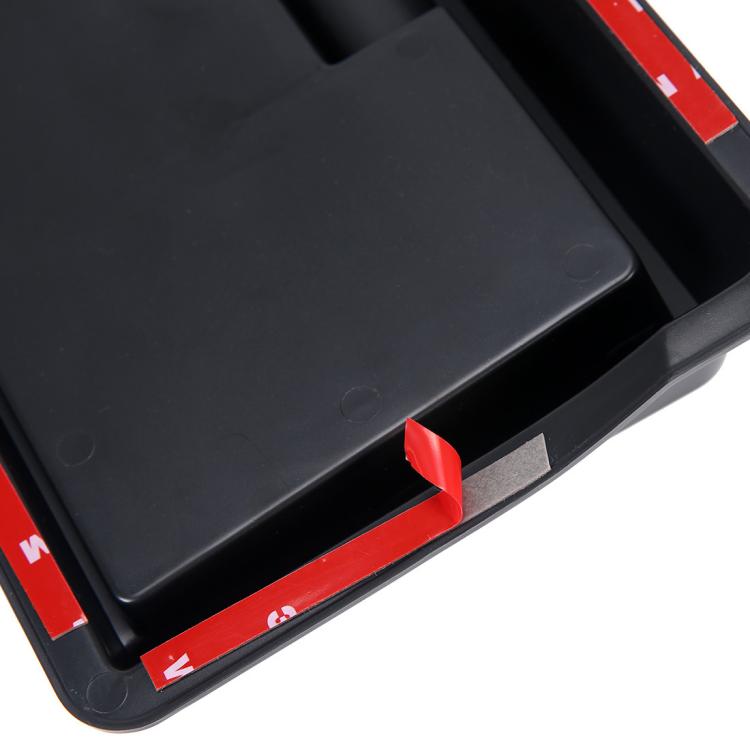 Black dashboard storage box corner with protective film tabs, close-up