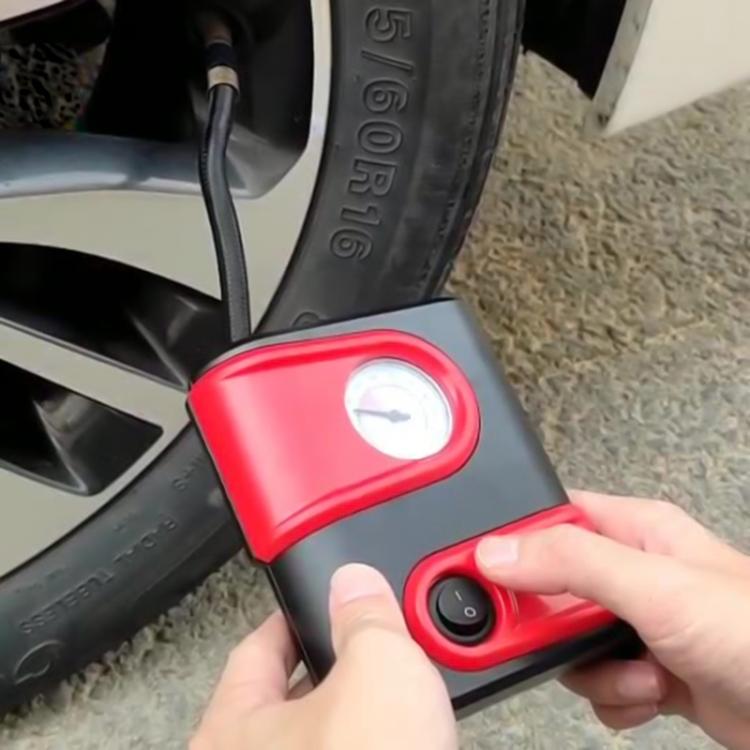 Red mini electric air pump with built-in gauge held near a car tire