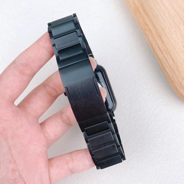 Black stainless steel watch band held upright, showing its broad center link and segmented ends.