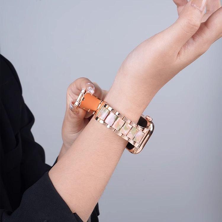 Rose gold metal watch band with pale pink resin links shown fastened on a wrist.