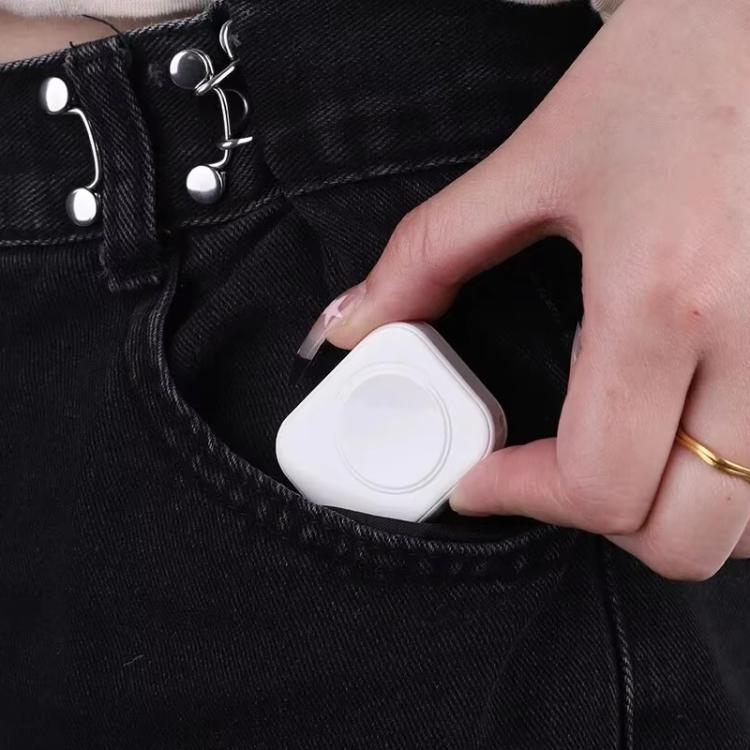 Compact white magnetic watch charger held beside a jeans pocket.