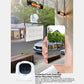 White security camera near a window with a smartphone showing the app view