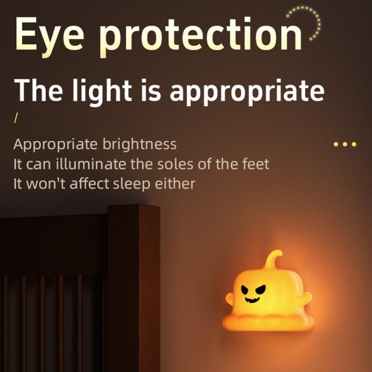 Small orange pumpkin ghost silicone night light, softly glowing in a dark room