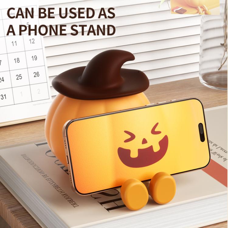 Silicone pumpkin night light used as a phone stand, jack-o’-lantern face, orange glow
