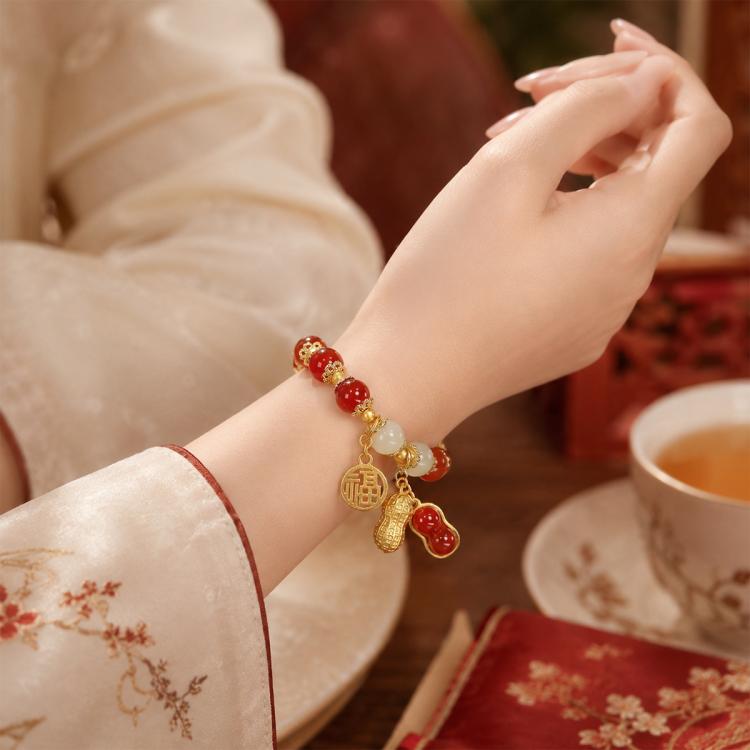Red bead bracelet on wrist with gold-tone coin and peanut charms and white bead accents