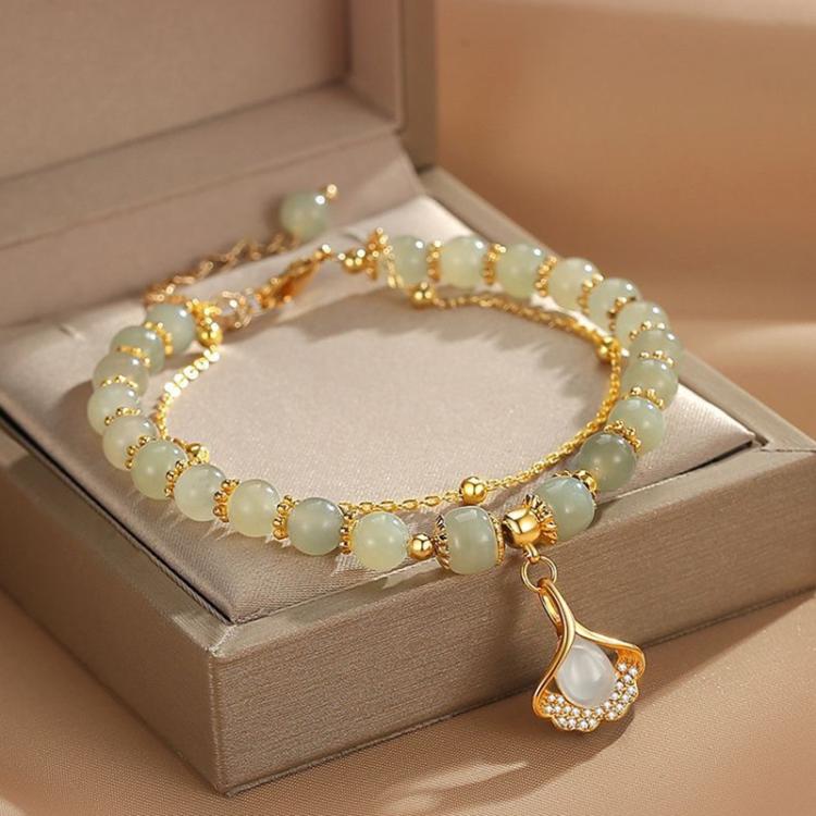 Gold charm bracelet with pale green beads and a teardrop leaf pendant charm.