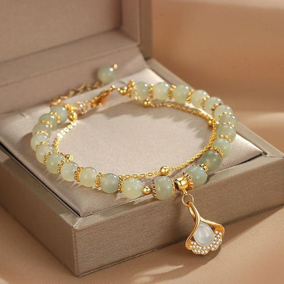 Gold charm bracelet with pale green beads and a teardrop leaf pendant charm.