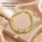 Gold-toned lightweight charm bracelet with pale green beads and a leaf pendant charm.
