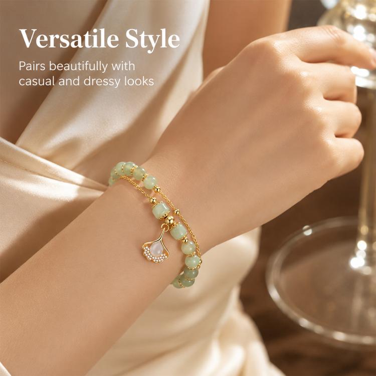 Gold beaded charm bracelet on wrist with pale green beads and a teardrop leaf pendant.