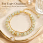 Gold beaded charm bracelet with pale green beads and a leaf pendant over a tray.