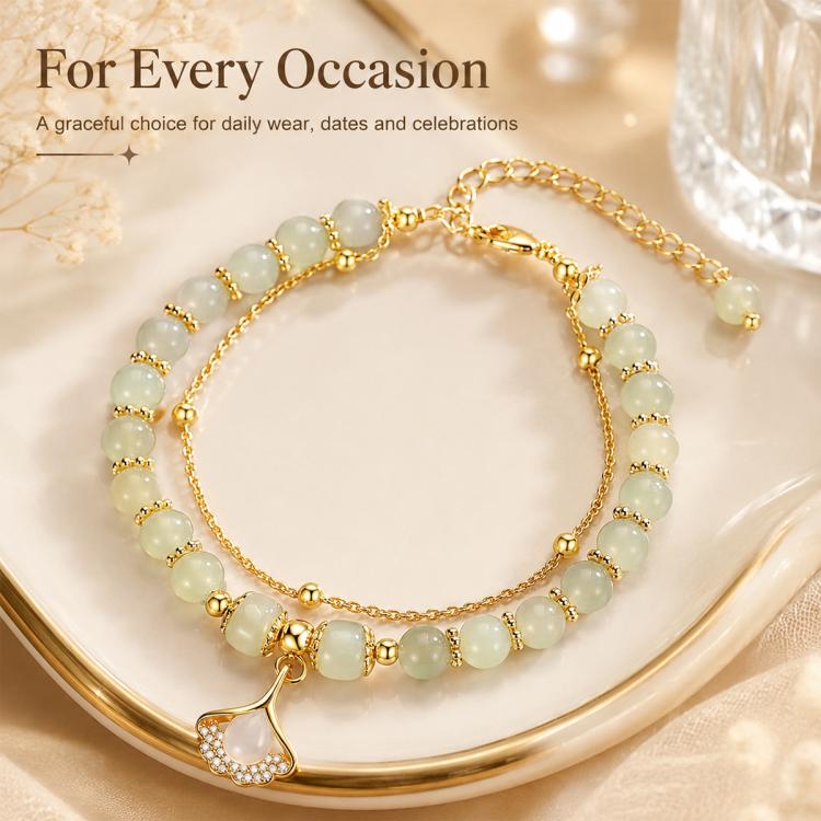 Gold beaded charm bracelet with pale green beads and a leaf pendant over a tray.