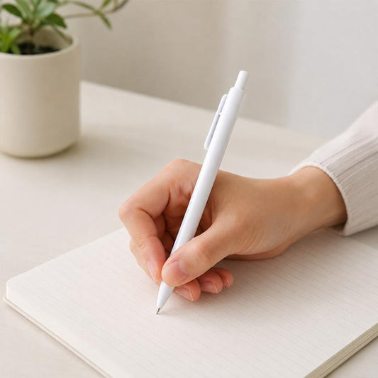 White retractable ballpoint pen with 0.7mm bullet tip, held over a lined notebook.