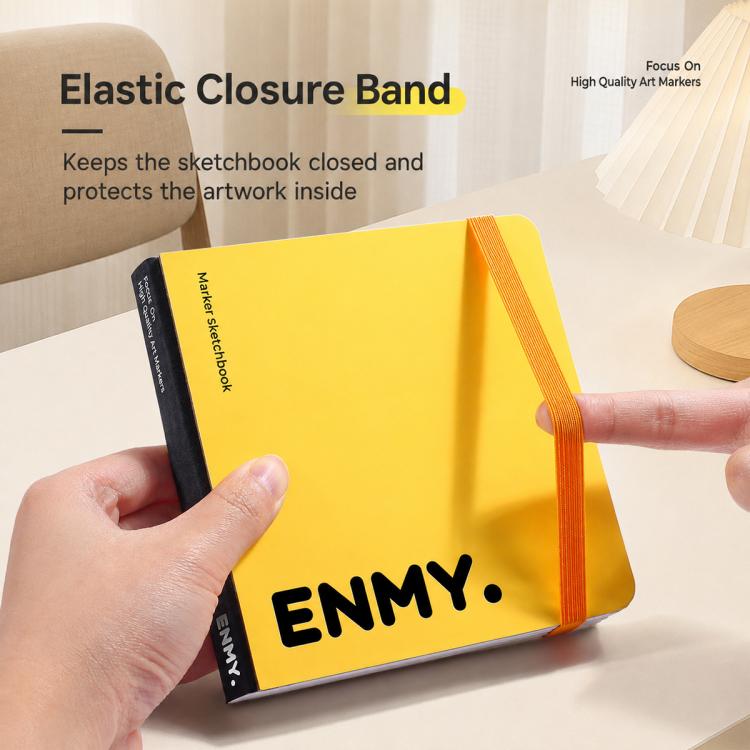 Yellow ENMY square sketchbook held by hand, with elastic closure band closed
