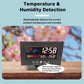Black LCD weather clock on wood with temperature and humidity readouts and weather icons.