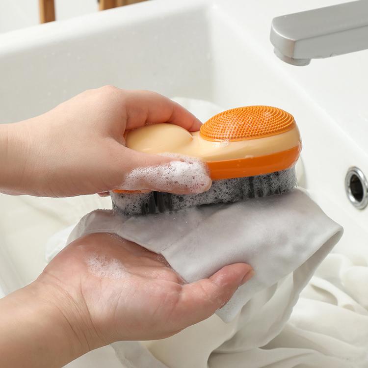 Orange double-sided laundry brush with foam scrubbing white fabric in sink