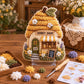 3D textile art cottage with honey-colored roof, flowers, and storefront sign