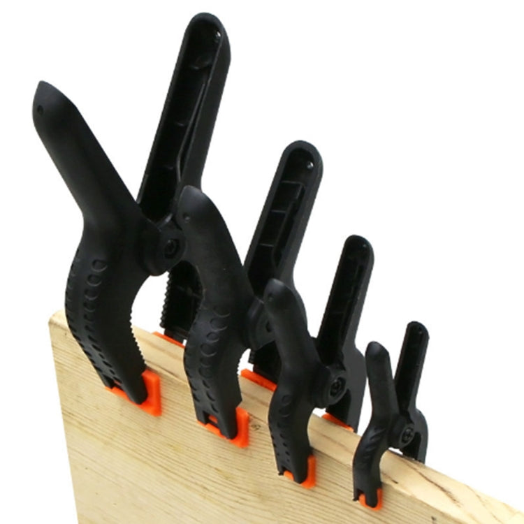 Five black spring clamps clipped to a wooden board for photo backdrops